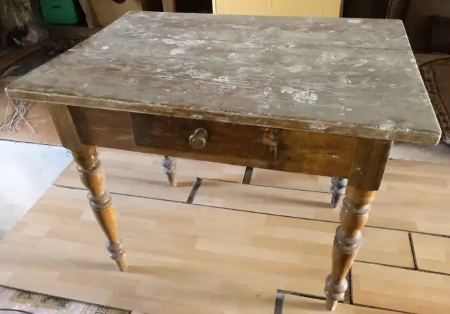Stary drewniany stół z szufladą, gotowy do renowacji. Blat jest zniszczony, ale nogi stołu są ozdobne.