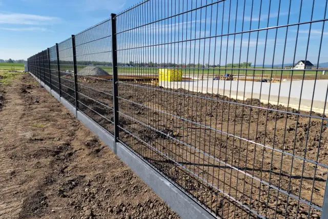 Nowy, metalowy płot panelowy z betonowym podmurówką na budowie.