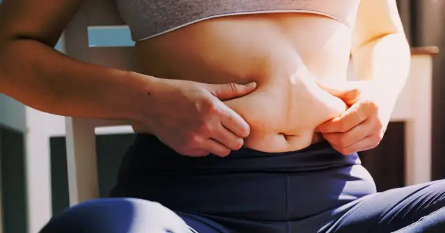 Kobieta chwyta fałd tłuszczu na brzuchu, zastanawiając się, jak schudnąć 4 kg.