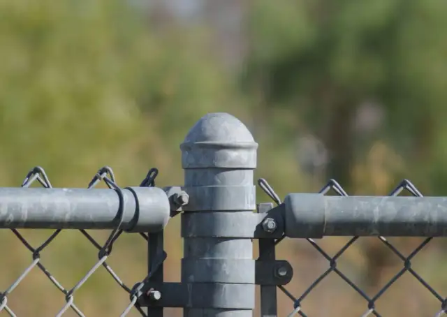 Detale montażu słupków ogrodzeniowych: metalowy słup z siatką i rurą poziomą.