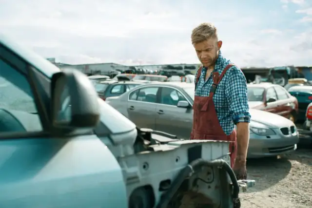 Pracownik złomowiska zastanawia się, ile zarabia handlarz samochodowy, patrząc na rozłożony samochód.