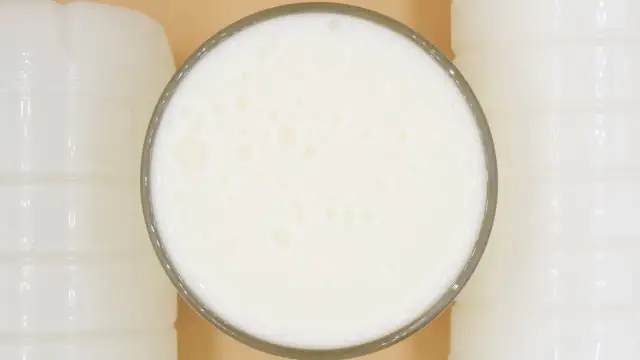 Szklanka pełna pianistego kefiru, otoczona białymi butelkami. Idealny moment, kiedy pić kefir, to teraz!