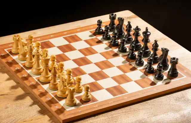 Drewniana szachownica z ustawionymi białymi i czarnymi figurami szachowymi.