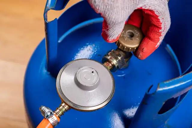 Ręka w rękawicy dokręca zawór na niebieskiej butli z gazem LPG.