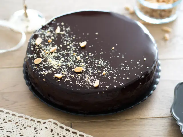 Błyszczący tort oblany czekoladą, posypany orzeszkami i okruszkami.