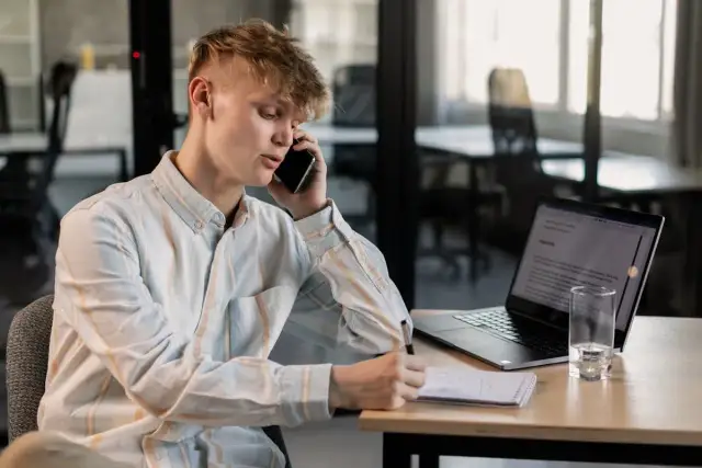 Młody mężczyzna rozmawia przez telefon, notując coś w zeszycie. Obok laptop i szklanka wody. Czy to numer 8012 co to za numer?