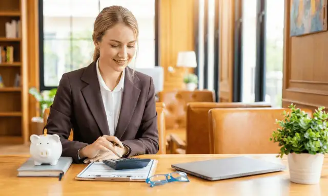Kobieta przy biurku z skarbonką świnką i kalkulatorem. Zastanawia się, otwarty fundusz emerytalny co to, jak najlepiej zainwestować.
