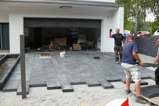 Budowa podjazdu z ciemnych płyt betonowych przed nowoczesnym budynkiem.