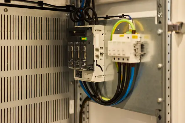 Wnętrze szafy elektrycznej z bezpiecznikami i przewodami. Sprawdź, jak sprawdzić czy falownik działa, analizując połączenia i wskaźniki.