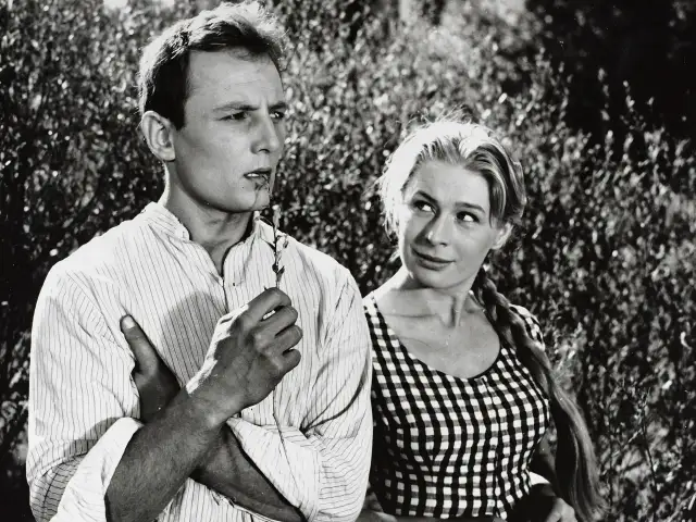 Młody mężczyzna, Eugeniusz Korczarowski, z gałązką w ustach, spogląda w bok. Obok niego uśmiechnięta kobieta w kratkę.