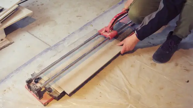 Ręce trzymające płytkę gresową na przecinarce do płytek.