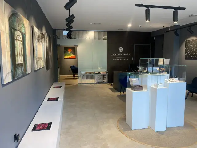 Wnętrze sklepu jubilerskiego z obrazami na ścianach i gablotami z biżuterią.