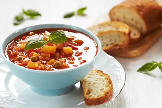 Zupa jarzynowa a minestrone w niebieskiej miseczce, udekorowana bazylią, podana z chrupiącym pieczywem.