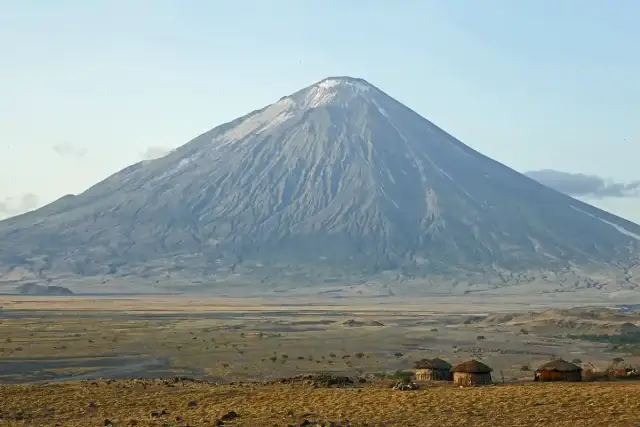 Ol Doinyo Lengai, wulkan w Tanzanii, góruje nad sawanną z kilkoma tradycyjnymi chatami Masajów.