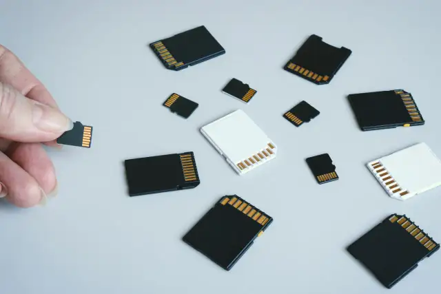 Dłoń trzyma kartę pamięci, obok leżą różne karty SD i microSD. Jaka karta pamięci do aparatu będzie najlepsza?