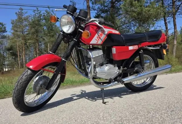 Czerwona Jawa TS 350, jeden z kultowych motocykli, gotowa na przejażdżkę po leśnej drodze.