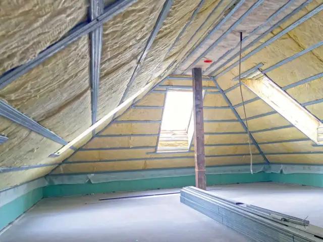 Strych w trakcie izolacji, z widoczną wełną mineralną i stelażem. Czy strych to powierzchnia użytkowa? Tu powstaje przestrzeń do życia.