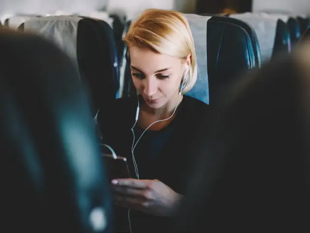 Kobieta w słuchawkach korzysta z telefonu, ciesząc się internetem w samolocie.