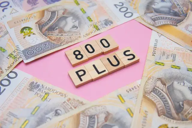 Drewniane klocki z napisami "800" i "PLUS" na tle polskich banknotów 200 zł.