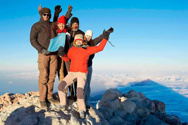 Grupa przyjaciół na szczycie wulkanu Teide, ciesząca się widokiem. Wejście na wulkan Teide zajmuje kilka godzin i wymaga zezwolenia.