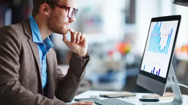 Mężczyzna w okularach analizuje wykresy na ekranie komputera, stosując zasady bezpiecznej pracy z komputerem.