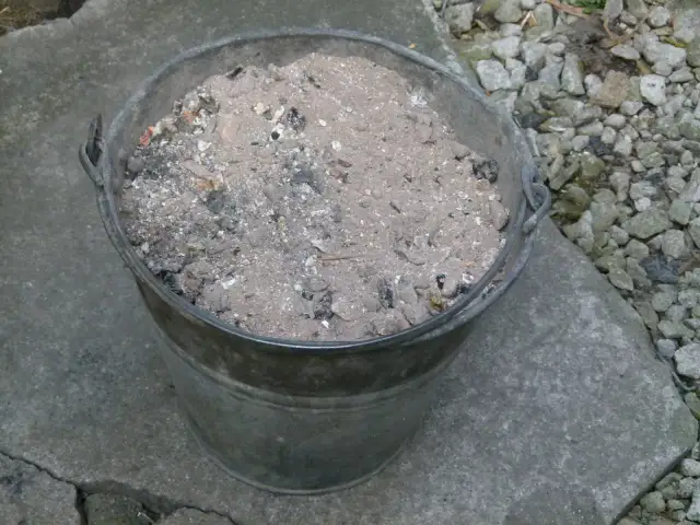 Metalowy kubeł wypełniony popiołem z węgla, który może posłużyć jako cenny nawóz do ogrodu.