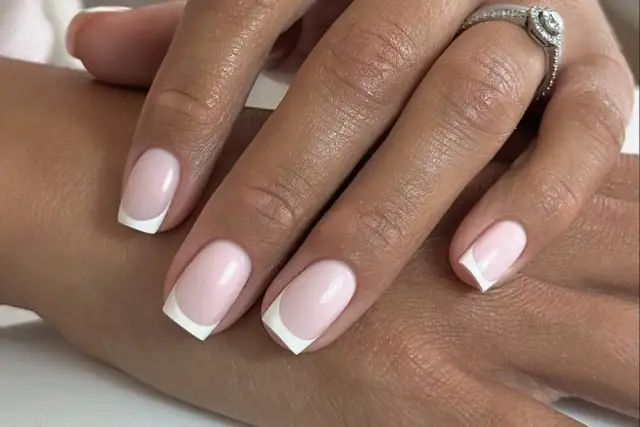 Delikatny french manicure z różowymi paznokciami, jak płatki kwiatów. Na serdecznym palcu błyszczący pierścionek.