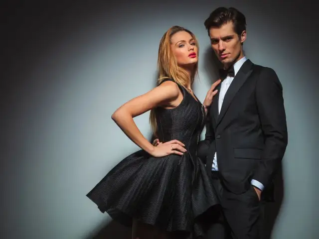 Elegancka para w strojach wieczorowych: kobieta w czarnej sukience, mężczyzna w smokingu.