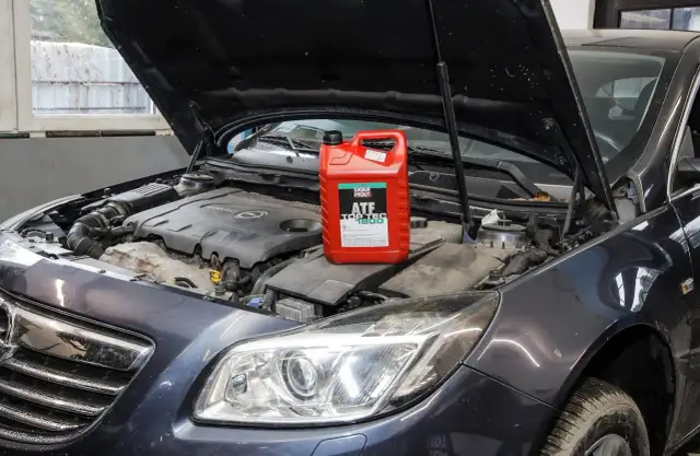 Czerwony kanister z płynem do automatycznych skrzyń biegów Liqui Moly ATF Top Tec 1800 na silniku samochodu.