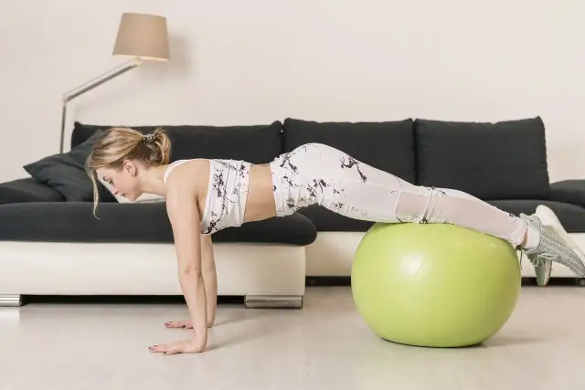 Kobieta wykonuje ćwiczenie na piłce gimnastycznej, które pomaga jak ćwiczyć na piłce żeby schudnąć.
