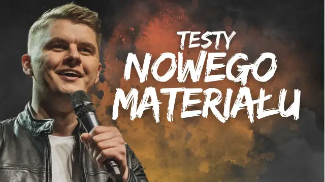 Uśmiechnięty komik na scenie, trzymający mikrofon. Na tle napis "TESTY NOWEGO MATERIAŁU".