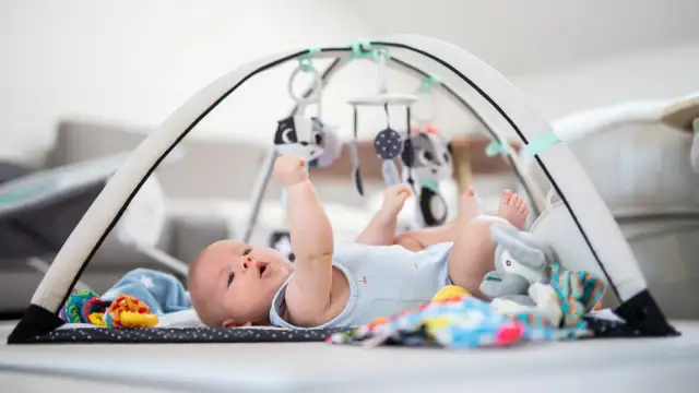 Niemowlę leży na macie sensorycznej pod łukiem z zabawkami.