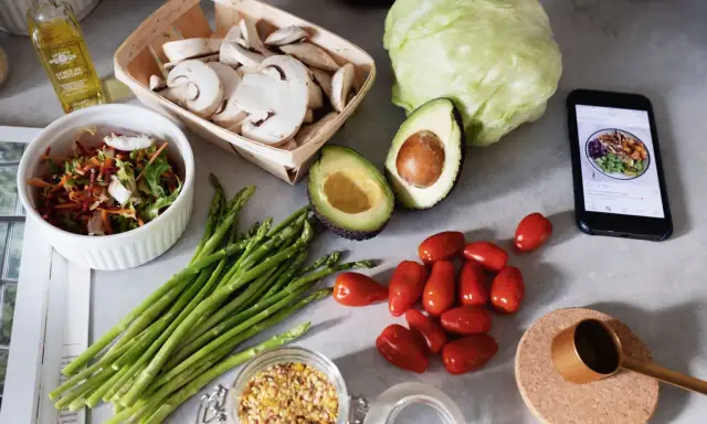 Świeże warzywa: awokado, szparagi, pomidorki, sałatka, pieczarki, kapusta, oliwa i telefon z posiłkiem.
