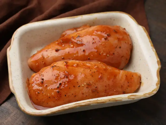 Dwa surowe filety z kurczaka w marynacie w naczyniu żaroodpornym.