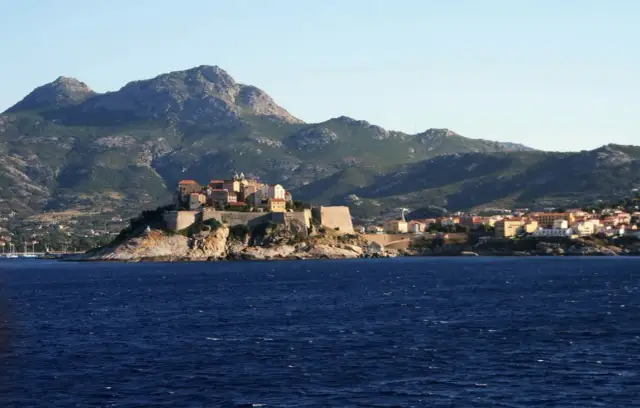 Widok na miasteczko na klifie z fortecą, w tle góry. Idealne miejsce na GR20 Korsyka.