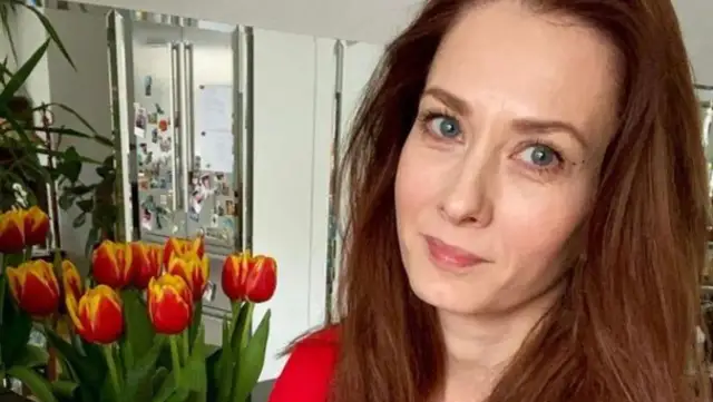 Anita Sokołowska wiek. Uśmiechnięta kobieta z rudymi włosami, w tle bukiet tulipanów i lustrzane szafki.