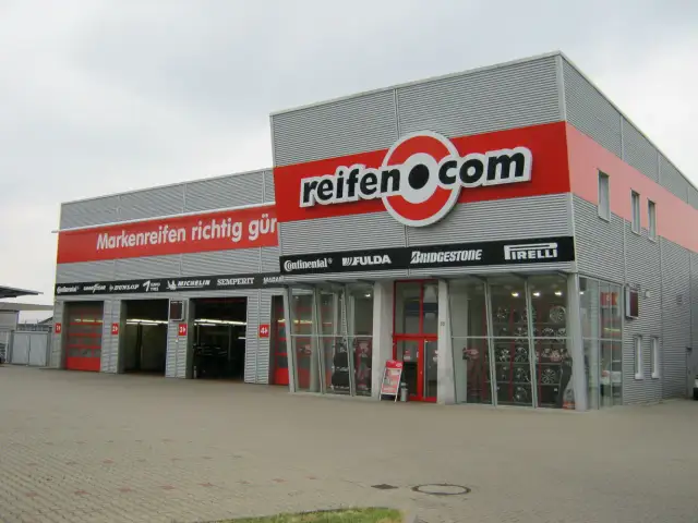 Fassade des reifen.com-Geschäfts mit roten Rolltoren und Reifenregalen im Fenster.