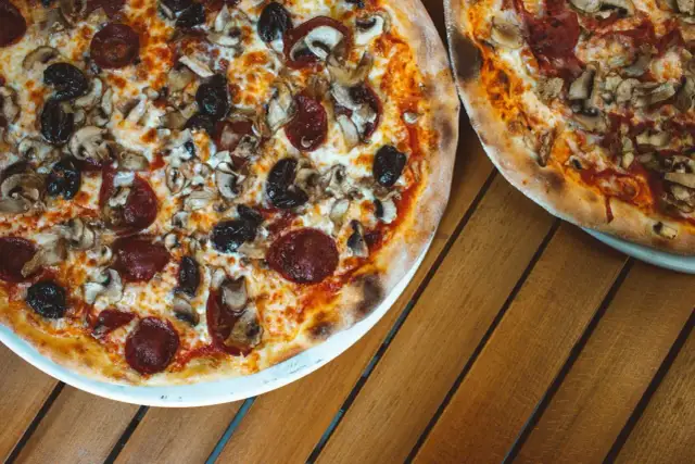 Dwie pizze z bogactwem składników na wierzchu: salami, pieczarki i czarne oliwki. Idealne na wspólny posiłek.