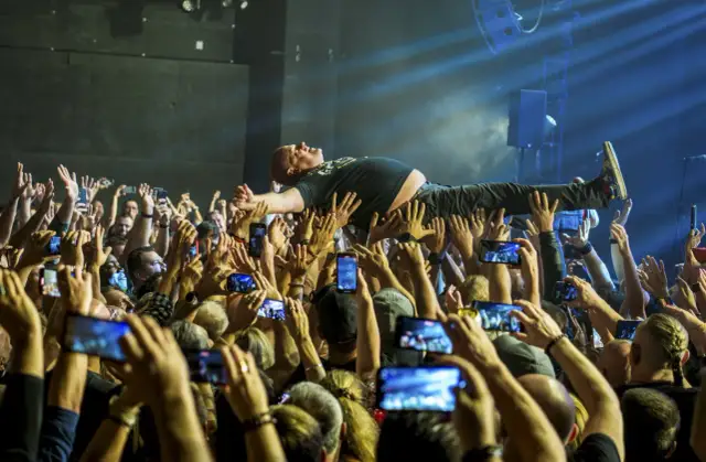 Kult w Arahji: wokalista zespołu niesiony przez tłum, fani nagrywają koncert telefonami.