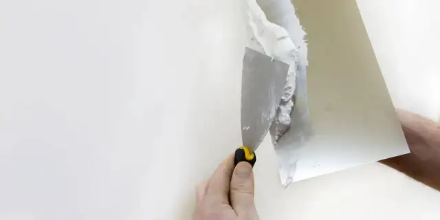 Dłoń z kielnią nakłada gips na białą ścianę.