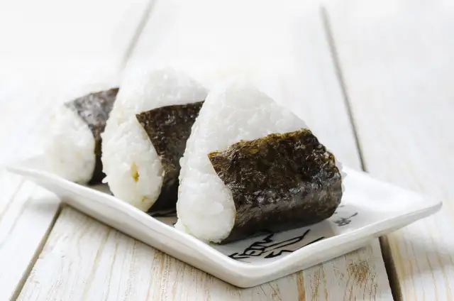 Trzy ryżowe kulki onigiri z nori na białym talerzyku. Idealne na szybki lunch, oto prosty onigiri przepis.