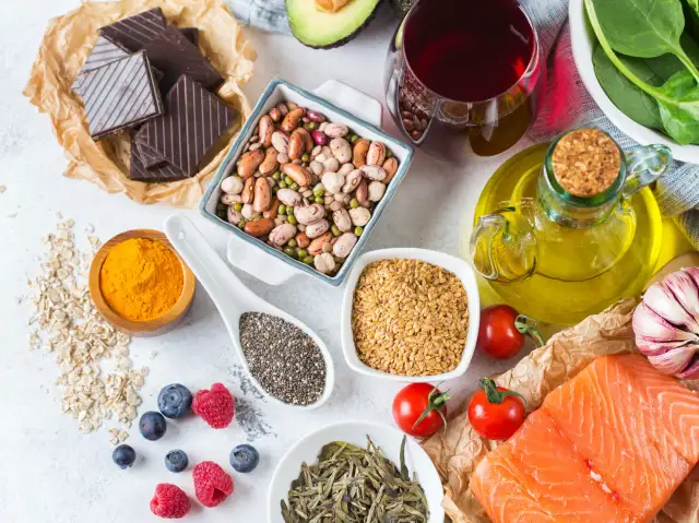 Zdjęcie przedstawia składniki zdrowe dla serca: łososia, awokado, jagody, fasolę, nasiona chia, siemię lniane, oliwę, czosnek, gorzką czekoladę i zieloną herbatę.