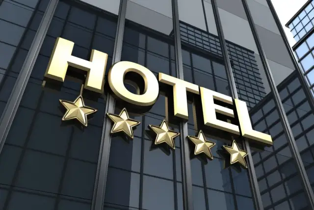 Złoty napis HOTEL z pięcioma gwiazdkami na tle nowoczesnego budynku hotelowego.