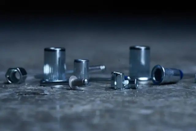 Różne rodzaje nitów i nakrętek nitowych leżą na betonowej powierzchni.