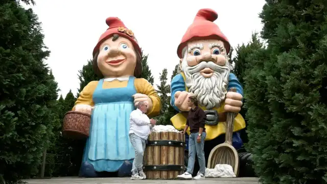 Dwie gigantyczne figurki krasnali ogrodowych, kobieta i mężczyzna, stoją pośród drzew.