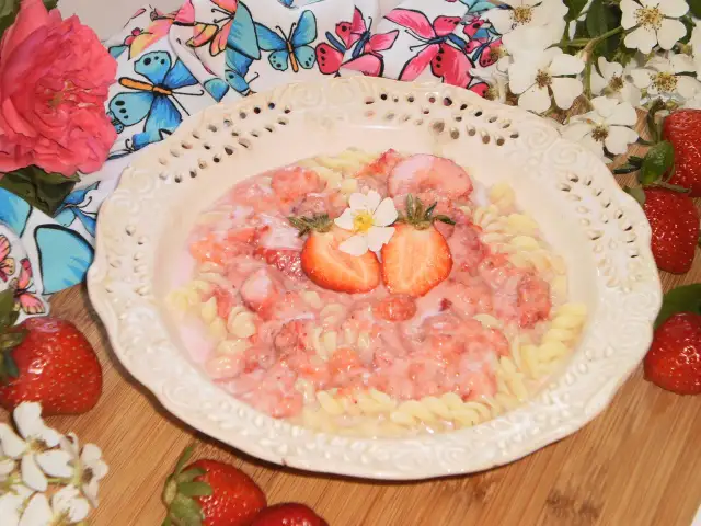 Makaron fusilli z sosem truskawkowym, udekorowany połówkami truskawek i kwiatkiem.