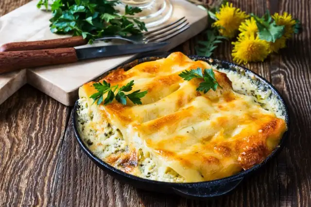 Złociste, zapieczone makaron cannelloni w sosie, udekorowane natką pietruszki, na drewnianym stole.