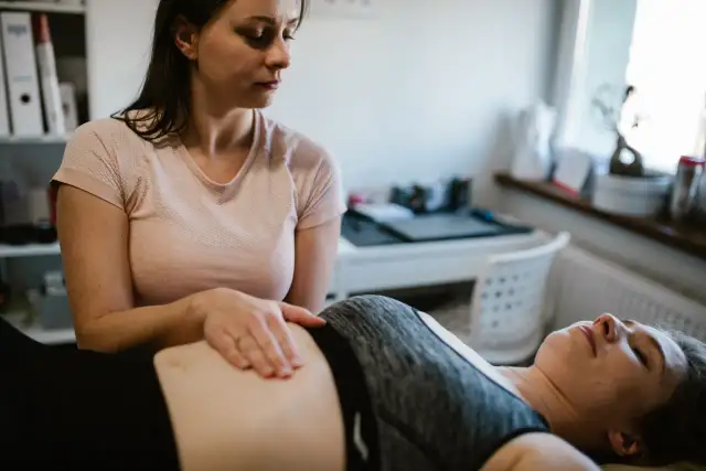Fizjoterapeutka wykonuje masaż brzucha pacjentce leżącej na kozetce.