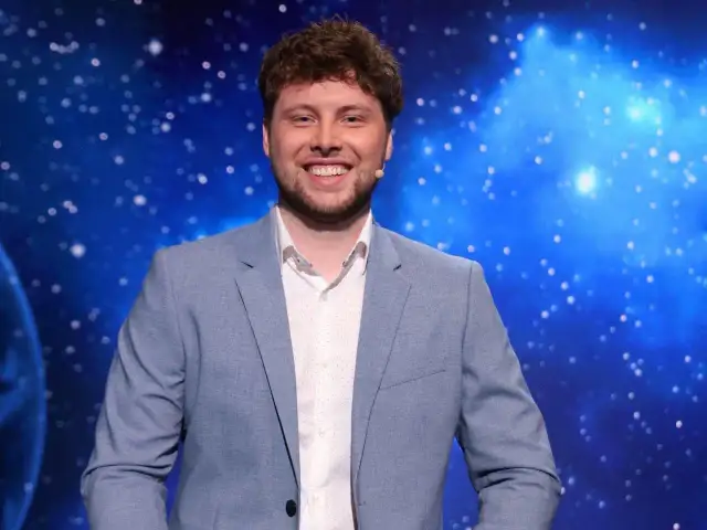 Uśmiechnięty mężczyzna w jasnej marynarce, jeden z dziesięciu jak się zgłosić, na tle kosmicznego nieba.