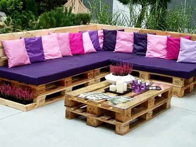 Narożna sofa i stolik kawowy z palet, ozdobione kolorowymi poduszkami i wrzosem. Prawdziwe cuda z palet!